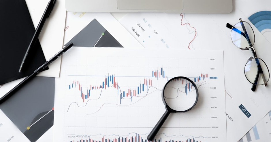 desk with financial charts, a magnifying glass, and eyeglasses